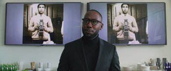 Movie still from “Yesterday” (2019), directed by Danny Boyle – A man in a black suit standing in front of two pictures; Medium shot, Over the shoulder angle