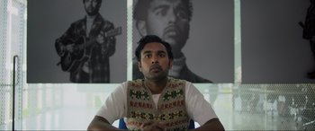 Movie still from “Yesterday” (2019), directed by Danny Boyle – A man sitting in front of a picture of himself; Medium shot, Low angle