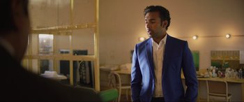 Movie still from “Yesterday” (2019), directed by Danny Boyle – A man in a blue suit standing in a room; Medium shot, Over the shoulder angle