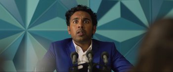 Movie still from “Yesterday” (2019), directed by Danny Boyle – A man in a blue suit is speaking at a podium; Close Up shot, Over the shoulder angle