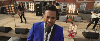 Movie still from “Yesterday” (2019), directed by Danny Boyle – A man in a blue jacket is singing into a microphone; Close Up shot, Over the shoulder angle
