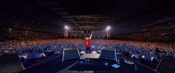 Movie still from “Yesterday” (2019), directed by Danny Boyle – A man standing on top of a stage in front of an audience; Extreme Wide shot, High angle