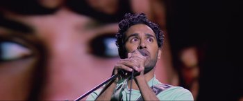Movie still from “Yesterday” (2019), directed by Danny Boyle – A man with curly hair is holding a microphone; Close Up shot, Over the shoulder angle
