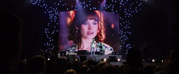 Movie still from “Yesterday” (2019), directed by Danny Boyle – A large screen showing a woman's face on a stage; Wide shot, Over the shoulder angle