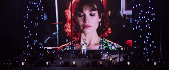 Movie still from “Yesterday” (2019), directed by Danny Boyle – A person standing on a stage in front of a large screen; Wide shot, Over the shoulder angle