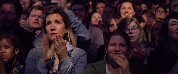 Movie still from “Yesterday” (2019), directed by Danny Boyle – A group of people sitting in front of each other with their hands over their mouths; Close Up shot, High angle