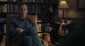 Movie still from “You Hurt My Feelings” (2023), directed by Nicole Holofcener – A man sitting in a chair in front of a bookcase; Medium shot, Over the shoulder angle