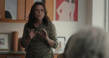 Movie still from “You Hurt My Feelings” (2023), directed by Nicole Holofcener – A woman in glasses is talking to a group of people in a room; Medium shot, Over the shoulder angle