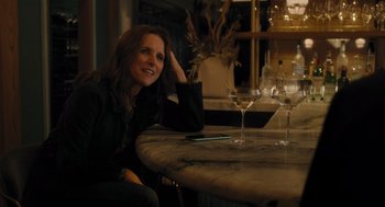 Movie still from “You Hurt My Feelings” (2023), directed by Nicole Holofcener – A woman sitting at a table in front of a wine glass; Medium shot, Over the shoulder angle