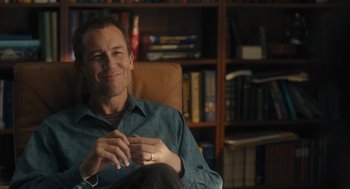 Movie still from “You Hurt My Feelings” (2023), directed by Nicole Holofcener – A man sitting in a chair in front of a book case; Medium shot, Over the shoulder angle