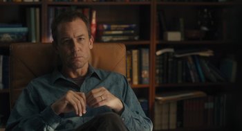 Movie still from “You Hurt My Feelings” (2023), directed by Nicole Holofcener – A man sitting in a chair in front of a book case; Medium shot, Over the shoulder angle