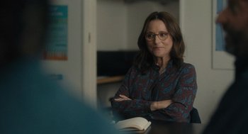 Movie still from “You Hurt My Feelings” (2023), directed by Nicole Holofcener – A woman sitting at a table with her arms crossed; Medium shot, Over the shoulder angle