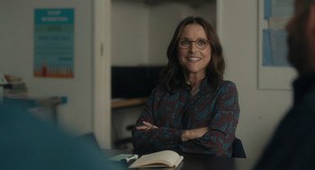 Movie still from “You Hurt My Feelings” (2023), directed by Nicole Holofcener – A woman sitting at a table with her arms crossed; Medium shot, Over the shoulder angle