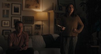 Movie still from “You Hurt My Feelings” (2023), directed by Nicole Holofcener – A woman standing in a living room holding a nintendo wii controller; Medium shot, Over the shoulder angle