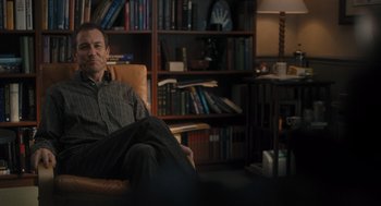 Movie still from “You Hurt My Feelings” (2023), directed by Nicole Holofcener – A man sitting in a chair in front of a bookshelf; Medium shot, Over the shoulder angle