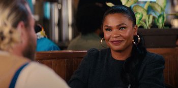 Movie still from “You People” (2023), directed by Kenya Barris – A woman sitting at a table smiling; Close Up shot, Over the shoulder angle