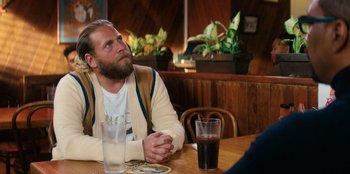Movie still from “You People” (2023), directed by Kenya Barris – A man sitting at a table with a glass of soda; Medium shot, Over the shoulder angle