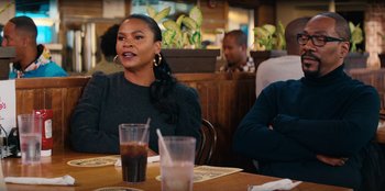 Movie still from “You People” (2023), directed by Kenya Barris – A woman sitting at a table in front of a glass of soda; Medium shot, Over the shoulder angle