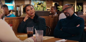 Movie still from “You People” (2023), directed by Kenya Barris – A woman sitting at a table in front of a glass of water; Medium shot, Over the shoulder angle