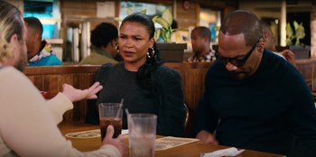 Movie still from “You People” (2023), directed by Kenya Barris – A woman sitting at a table in front of a glass of water; Medium shot, Over the shoulder angle