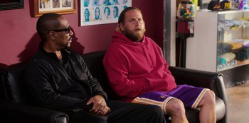 Movie still from “You People” (2023), directed by Kenya Barris – Two men sitting on a couch in front of a wall; Medium shot, Over the shoulder angle