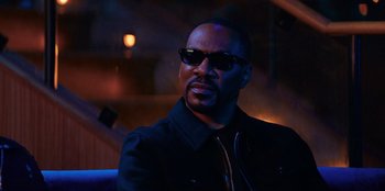 Movie still from “You People” (2023), directed by Kenya Barris – A man wearing sunglasses sitting in a dark room; Close Up shot, Over the shoulder angle
