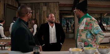 Movie still from “You People” (2023), directed by Kenya Barris – A man standing next to two other men in front of a wooden wall; Medium shot, Over the shoulder angle