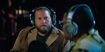 Movie still from “You People” (2023), directed by Kenya Barris – A man with a beard wearing headphones and a brown jacket; Close Up shot, Over the shoulder angle
