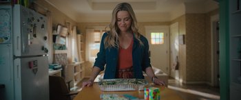 Movie still from “Your Place or Mine” (2023), directed by Aline Brosh McKenna – A woman standing in front of a box of food on top of a wooden table; Medium shot, Over the shoulder angle