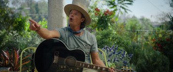Movie still from “Your Place or Mine” (2023), directed by Aline Brosh McKenna – A man with a hat playing a guitar outside; Close Up shot, Over the shoulder angle