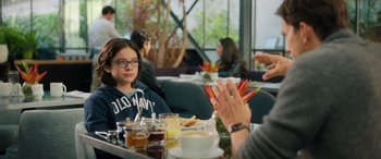 Movie still from “Your Place or Mine” (2023), directed by Aline Brosh McKenna – A young girl sitting at a table in front of other people; Medium shot, Over the shoulder angle
