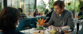 Movie still from “Your Place or Mine” (2023), directed by Aline Brosh McKenna – A man sitting at a table with a vase of flowers; Medium shot, Over the shoulder angle