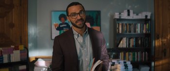 Movie still from “Your Place or Mine” (2023), directed by Aline Brosh McKenna – A man in a brown jacket holding a stack of books; Medium shot, Over the shoulder angle