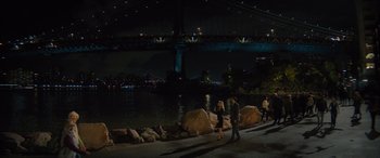 Movie still from “Your Place or Mine” (2023), directed by Aline Brosh McKenna – A group of people walking along a sidewalk near a body of water at night; Extreme Wide shot, High angle
