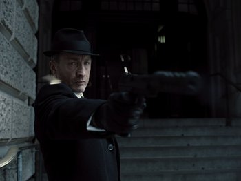 Movie still from “Zack Snyder's Justice League” (2021), directed by Zack Snyder – A man in a black suit and a black hat holding a gun; Close Up shot, Low angle