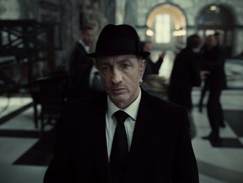Movie still from “Zack Snyder's Justice League” (2021), directed by Zack Snyder – A man wearing a suit and a black hat; Close Up shot, Low angle