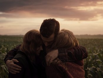 Three people hugging in a field at sunset