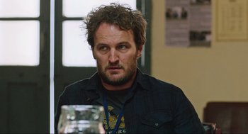 Movie still from “Zero Dark Thirty” (2012), directed by Kathryn Bigelow – A person sitting at a table with a glass; Close Up shot, Over the shoulder angle