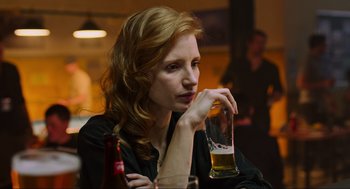Movie still from “Zero Dark Thirty” (2012), directed by Kathryn Bigelow – A woman sitting at a table holding a glass of beer; Close Up shot, Over the shoulder angle