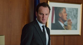 Movie still from “Zero Dark Thirty” (2012), directed by Kathryn Bigelow – A man in a suit and tie standing in front of a portrait; Close Up shot, Over the shoulder angle