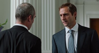 Movie still from “Zero Dark Thirty” (2012), directed by Kathryn Bigelow – A man in a suit and tie standing next to another man in a suit and tie; Medium shot, Over the shoulder angle