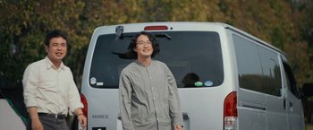 Movie still from “Zom 100: Bucket List of the Dead” (2023), directed by Yûsuke Ishida – A man standing in front of a white van; Medium shot, Low angle