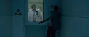 Movie still from “Zombieland: Double Tap” (2019), directed by Ruben Fleischer – A man in a white lab coat looking out of a window; Medium shot, Over the shoulder angle