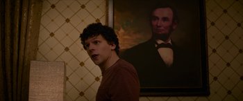 Movie still from “Zombieland: Double Tap” (2019), directed by Ruben Fleischer – A man standing in front of a painting of abraham lincoln; Medium shot, Over the shoulder angle