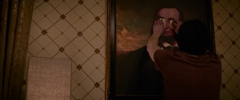 Movie still from “Zombieland: Double Tap” (2019), directed by Ruben Fleischer – A man holding his hand up to his face in front of a painting; Medium shot, Over the shoulder angle