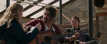 Movie still from “Zombieland: Double Tap” (2019), directed by Ruben Fleischer – A man playing a guitar while a woman watches; Medium shot, Over the shoulder angle