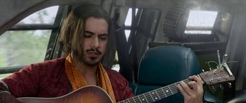 Movie still from “Zombieland: Double Tap” (2019), directed by Ruben Fleischer – A man sitting in a car playing a guitar; Medium shot, Over the shoulder angle