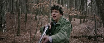 Movie still from “Zombieland: Double Tap” (2019), directed by Ruben Fleischer – A young man holding a rifle in a wooded area; Medium shot, Over the shoulder angle