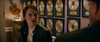 Movie still from “Zombieland: Double Tap” (2019), directed by Ruben Fleischer – A woman sitting in front of a row of gold records; Close Up shot, Over the shoulder angle