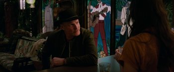 Movie still from “Zombieland: Double Tap” (2019), directed by Ruben Fleischer – A man sitting at a table in front of a stained glass window; Medium shot, Over the shoulder angle
